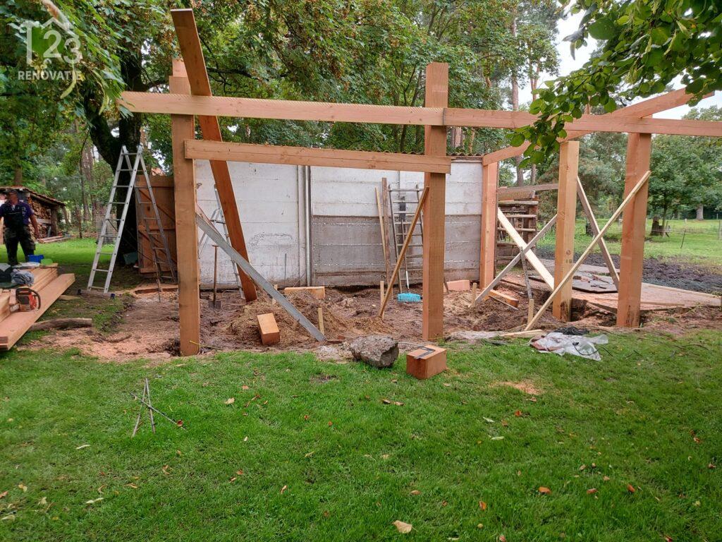 Een vakman plaatst het houten geraamte voor een nieuwe overkapping in een groene tuin als onderdeel van de buitenaanleg.